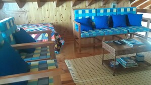 A cozy room with a wooden ceiling, a sofa with blue cushions, a patterned rug, and a small table with books and a cup.