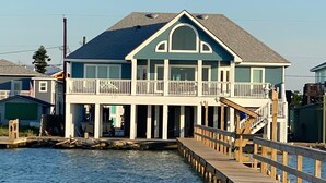 A waterfront house with a wooden deck extending over the water, a balcony, and a garage. - Sunset Cove-4 BR, 2 1/2 BA Waterfront Home. Sleeps 12-Private pier! (Rockport)