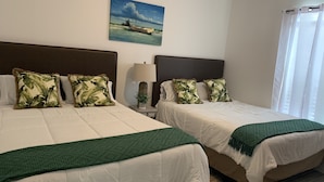 A hotel room with two beds, each with white bedding and green throw blankets. There is a painting of a boat on the wall, a lamp on the nightstand, and a window with white curtains. - Sunset Cove-4 BR, 2 1/2 BA Waterfront Home. Sleeps 12-Private pier! (Rockport)