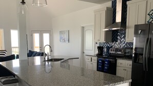 A modern kitchen with a large island, white cabinetry, stainless steel appliances, and pendant lighting. - Sunset Cove-4 BR, 2 1/2 BA Waterfront Home. Sleeps 12-Private pier! (Rockport)