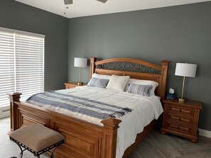 Quarto com cama de madeira, duas mesas de cabeceira com abajures, um banco e uma janela com persianas.