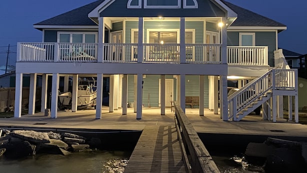A two-story waterfront house with a balcony, a dock, and a staircase leading to the upper level. - Sunset Cove-4 BR, 2 1/2 BA Waterfront Home. Sleeps 12-Private pier! (Rockport)