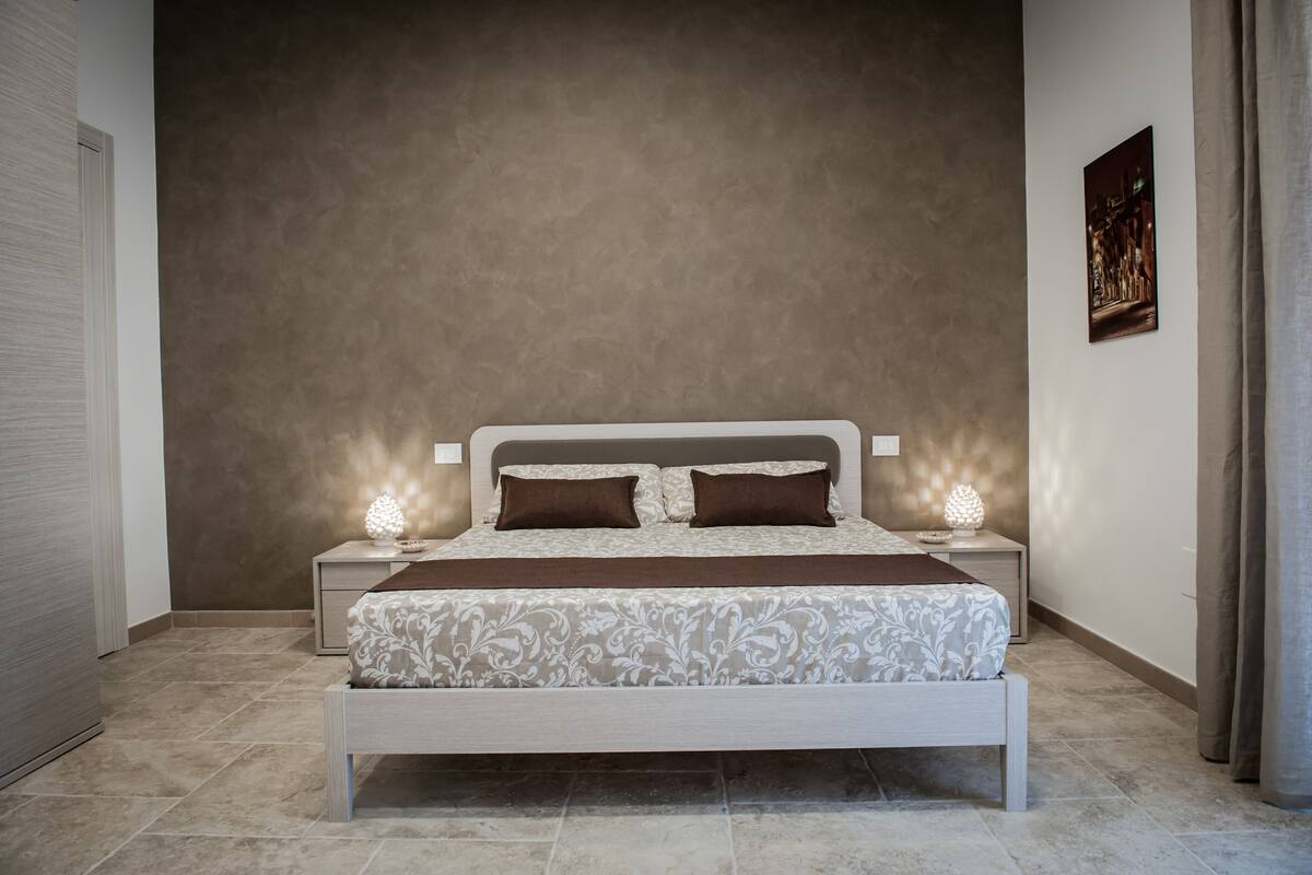 Quarto com cama, mesas de cabeceira e um quadro na parede.