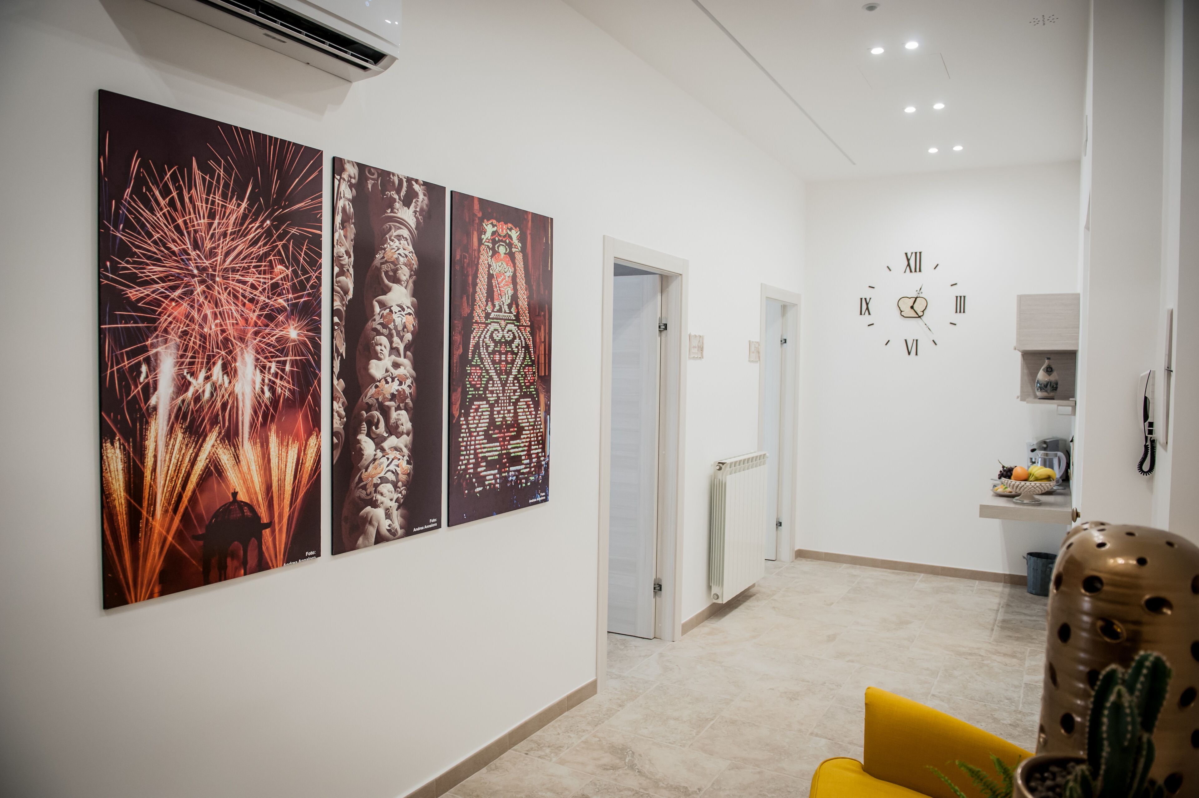 Un pasillo con tres grandes obras de arte colgadas en la pared, que representan fuegos artificiales y diseños tradicionales. Se observa un reloj en la pared, y un sillón con estampado de cactus en primer plano.