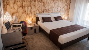 Une chambre moderne avec une tête de lit en bois, un grand lit recouvert d’une couverture marron, un bureau avec un ordinateur portable et une chaise.