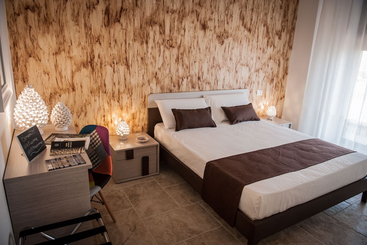 Quarto moderno com cabeceira de madeira, uma cama grande com colcha marrom, uma escrivaninha com um laptop e uma cadeira.