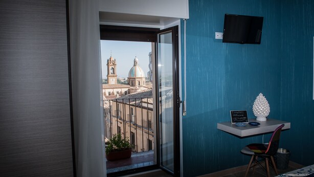 Une pièce avec un balcon, une plante en pot, un bureau avec une pancarte et un téléviseur fixé au mur.