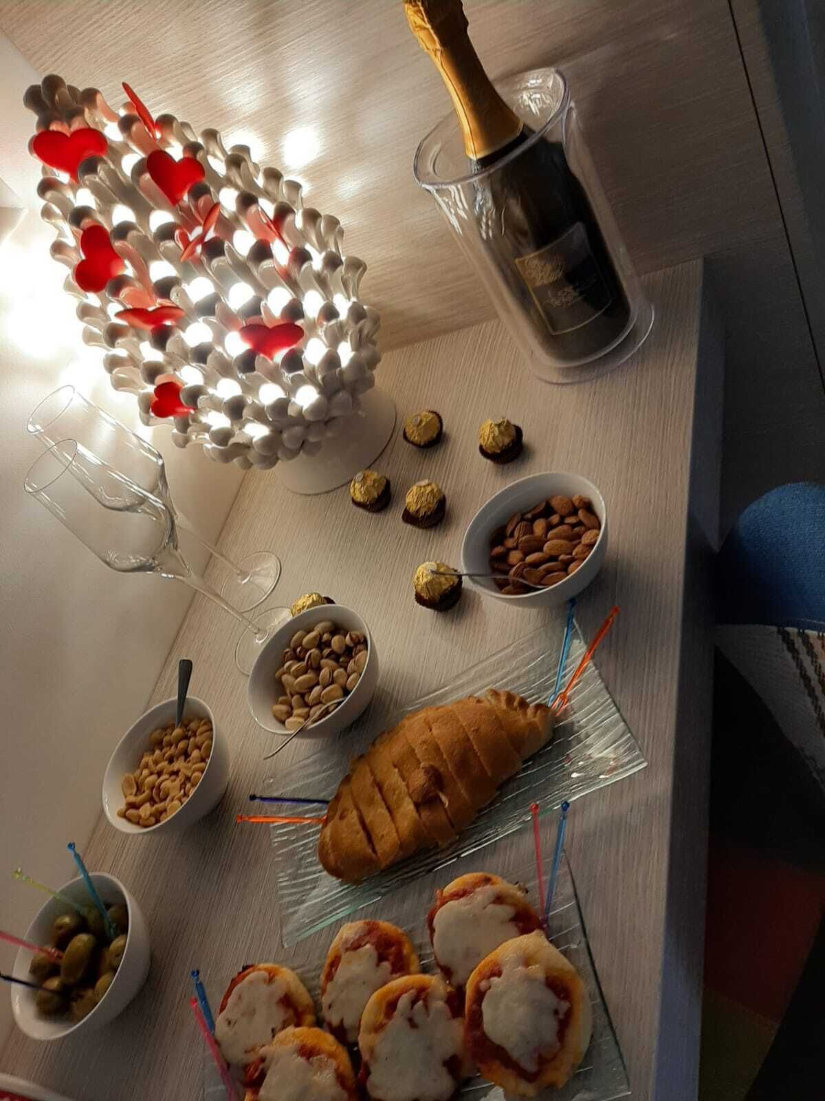 A table with a variety of snacks, including cookies, nuts, and a loaf of bread, along with a bottle of champagne.