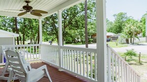 A covered porch with a ceiling fan, white railings, and a view of a residential area with trees and houses. - Beautiful Beach Getaway! Walk to Beach! Sleeps 6. (Oak Island)
