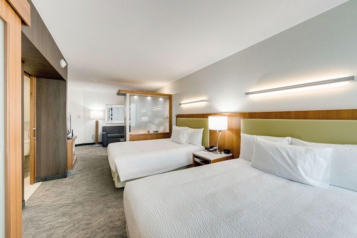 A hotel room with two beds, a desk, a chair, a mirror, and a nightstand.