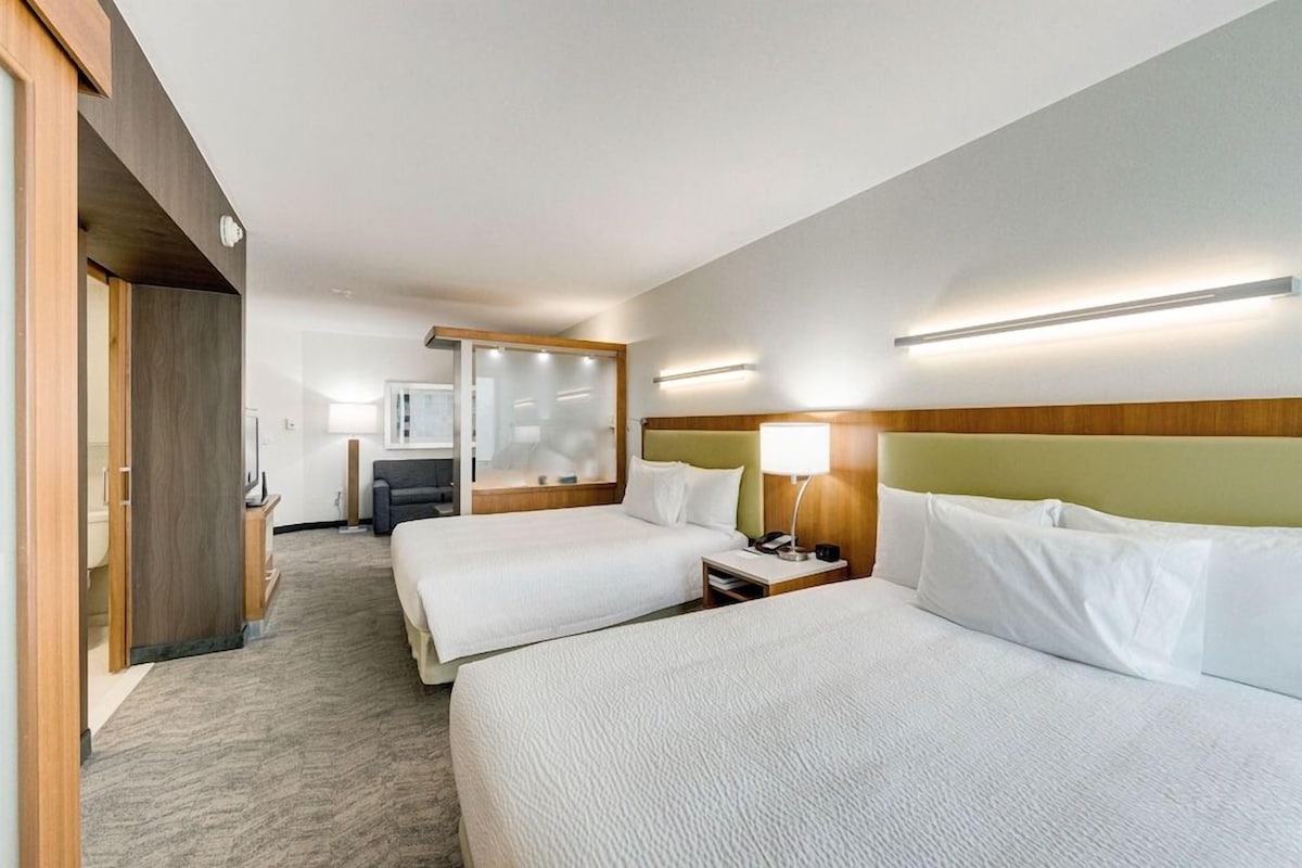 A hotel room with two beds, a desk, a chair, a mirror, and a nightstand.