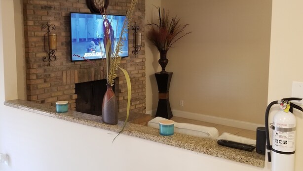 Un salon avec une cheminée en briques, un téléviseur fixé au-dessus et un extincteur accroché au mur.