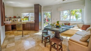 Una cucina moderna con isola centrale, una zona pranzo con tavolo apparecchiato per quattro persone e un angolo salotto con divano e cuscini.