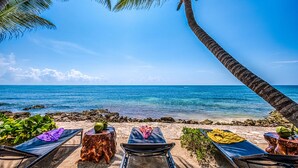 Una spiaggia con lettini, un tavolo di legno con dei cocco e vista sull'oceano.