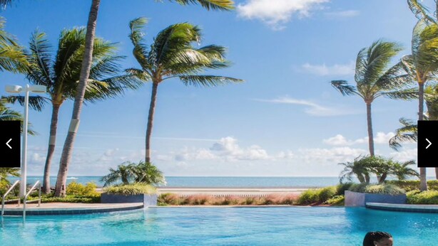 Une piscine à l’eau d’un bleu cristallin, entourée de palmiers et offrant une vue sur l’océan.