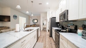 A modern kitchen with white cabinets, a marble countertop, and stainless steel appliances. - Short walk to Beach - Pool -Sleeps 8 Wifi (Gulf Shores)