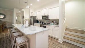 A modern kitchen with white cabinetry, a marble island, and wooden stools. - Short walk to Beach - Pool -Sleeps 8 Wifi (Gulf Shores)