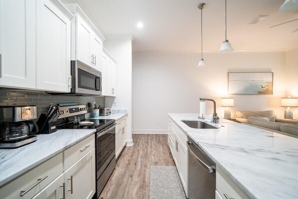 A modern kitchen with white cabinets, a microwave, a coffee maker, and a sink.