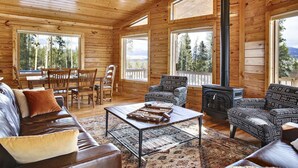 Ein gemütliches Blockhaus-Interieur mit Holzwänden, einer Essecke, einer Couch, einem gemusterten Sessel und einem Kamin.