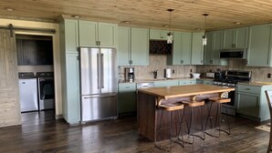 Una cocina moderna con armarios verde claro, electrodomésticos de acero inoxidable, una isla de madera con taburetes altos y techo de madera.