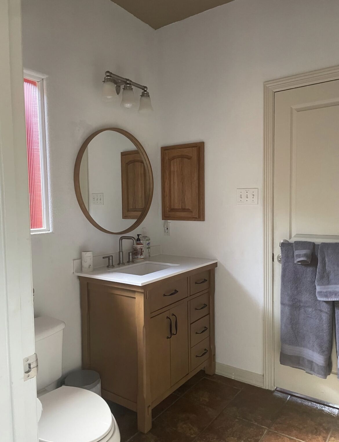 Une salle de bain avec des toilettes, un lavabo avec un miroir, des meubles en bois et une serviette accrochée à la porte.