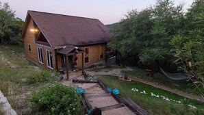 Een houten huis met schuin dak, een veranda met leuning en een tuin met hangmat.