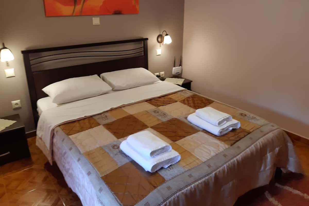 A neatly made bed with a quilt and two folded towels, a nightstand with a lamp, and a wall-mounted light fixture.