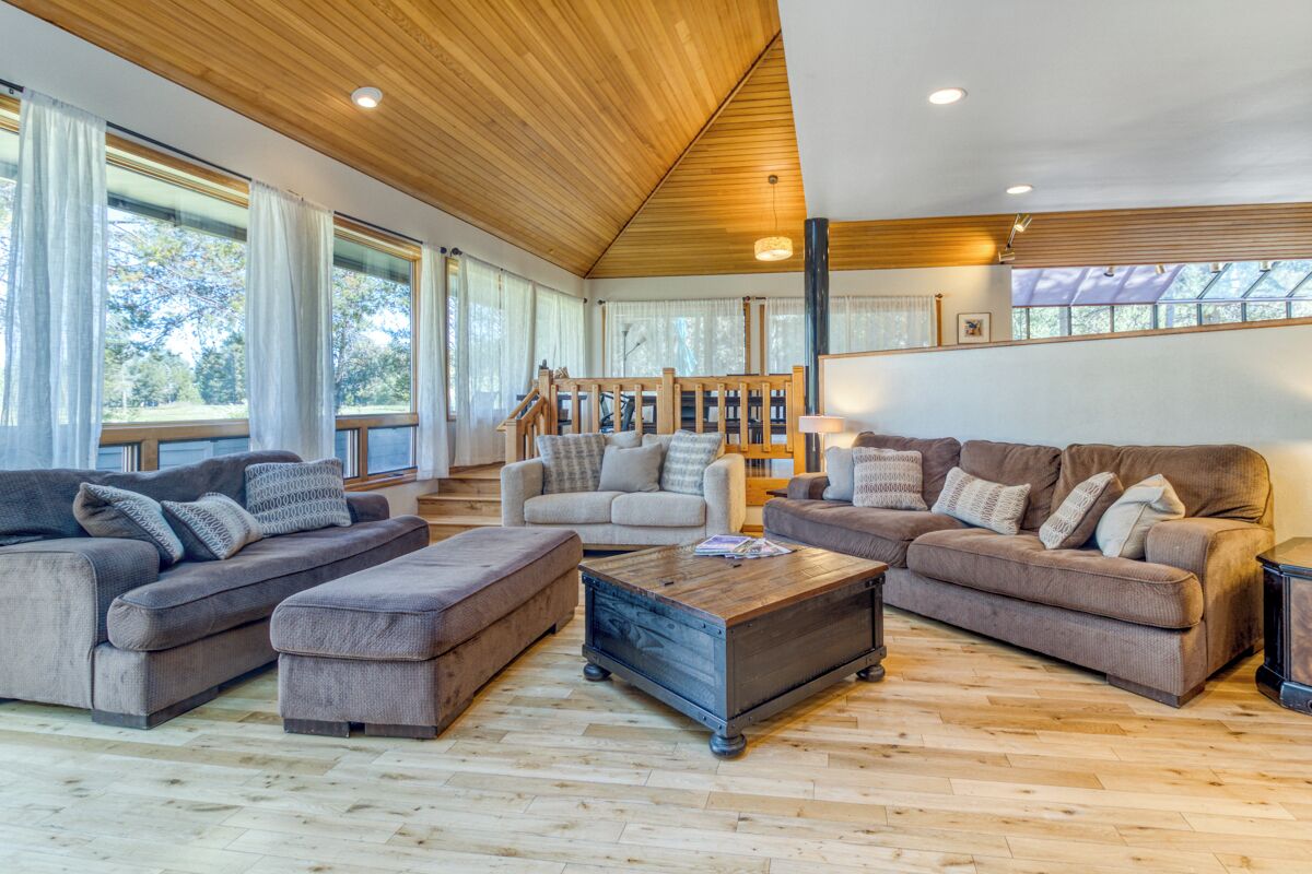 A spacious living room with a high ceiling and wooden beams, featuring a large sofa set, a coffee table, and a staircase leading to an upper level.