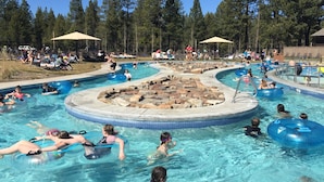 Ein Schwimmbecken mit mehreren Bahnen, umgeben von Liegestühlen und Sonnenschirmen, eingebettet in eine bewaldete Landschaft.