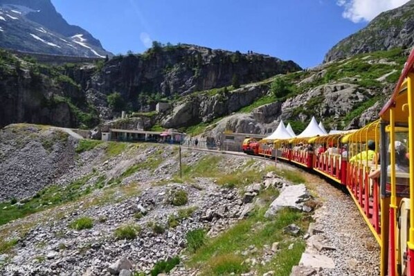 A train with yellow and red cars traveling through a mountainous area with rocky terrain and tents in the background. - HOLIDAY IN QUIET AT THE MOUNTAIN (Issor)