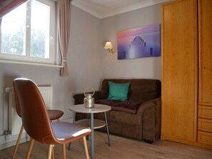 A cozy room with a brown leather sofa, a small round table, a lamp, and a wooden wardrobe.