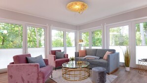 A spacious living room with a grey sofa, a pink armchair, and a round coffee table. - Tide App. 3 gold right (Ostseebad Boltenhagen)