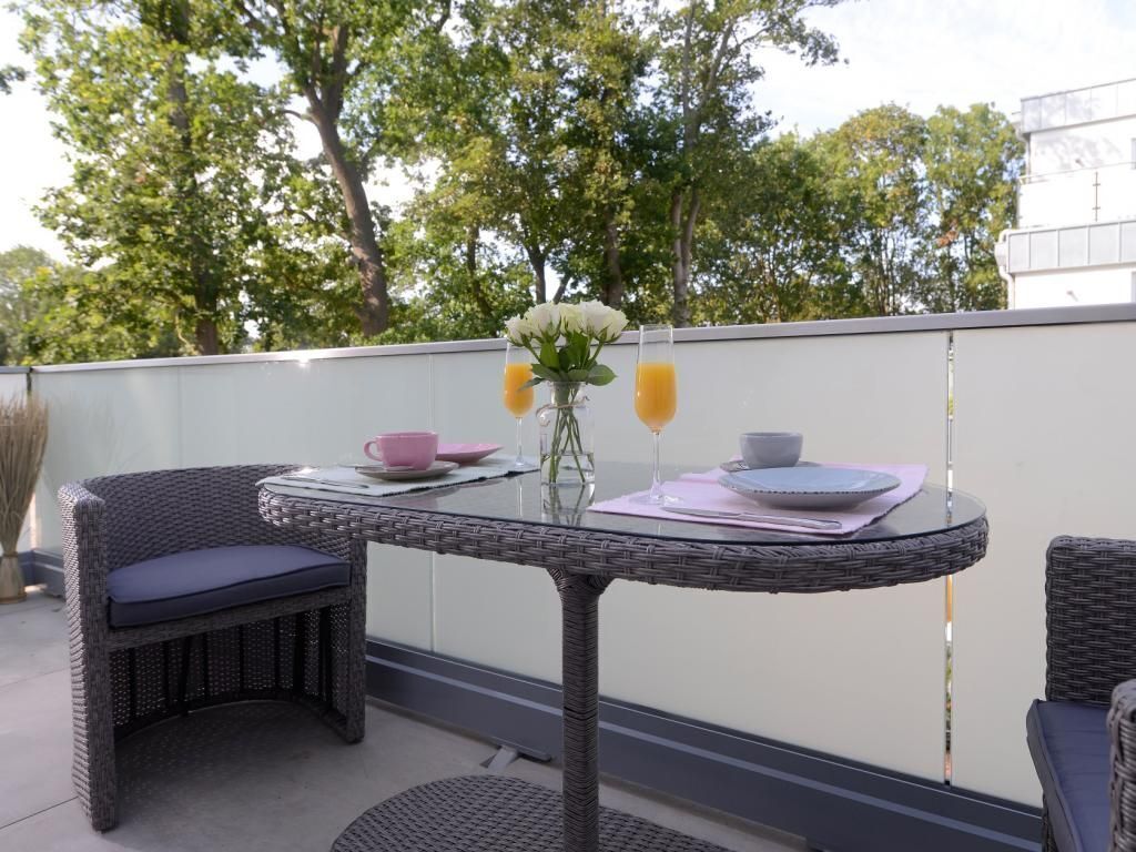 Ein Balkon mit Korbmöbeln, einem Glastisch und einer Vase mit Blumen.
