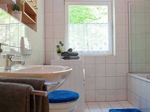 A bathroom with two sinks, a window, a shower, and a blue bath mat.