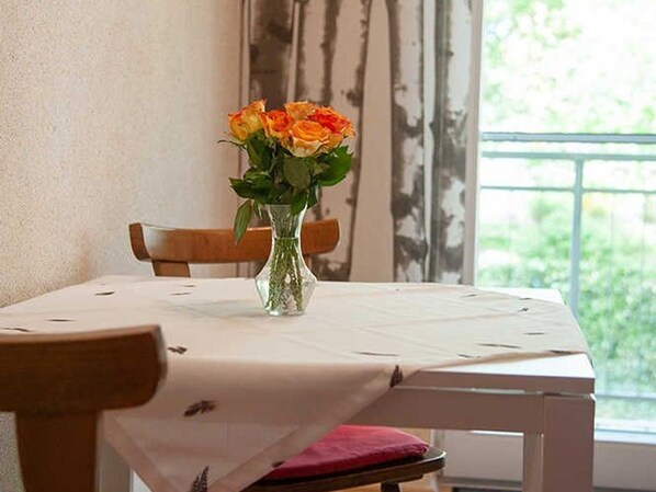 A dining table with a vase of flowers, a chair, and a window with a view of greenery.