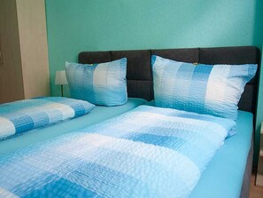 A bed with a blue and white checkered bedspread and matching pillows, a dark headboard, and a nightstand with a lamp.