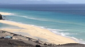 Un paisaje costero con playa arenosa, mar tranquilo y montañas al lejano.