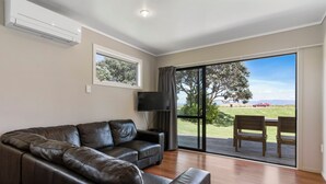 A modern living room with a leather sofa, a flat-screen TV, and a large sliding glass door leading to an outdoor area with a table and chairs. - Comfort Inn Sunset (Thames)