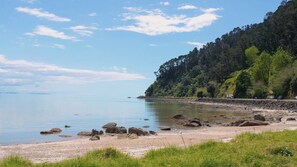 A coastal landscape with a sandy beach, calm water, and a forested hillside.