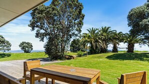 A wooden deck with a table and chairs, surrounded by lush greenery and palm trees, overlooking a grassy area with a clear sky. - Comfort Inn Sunset (Thames)