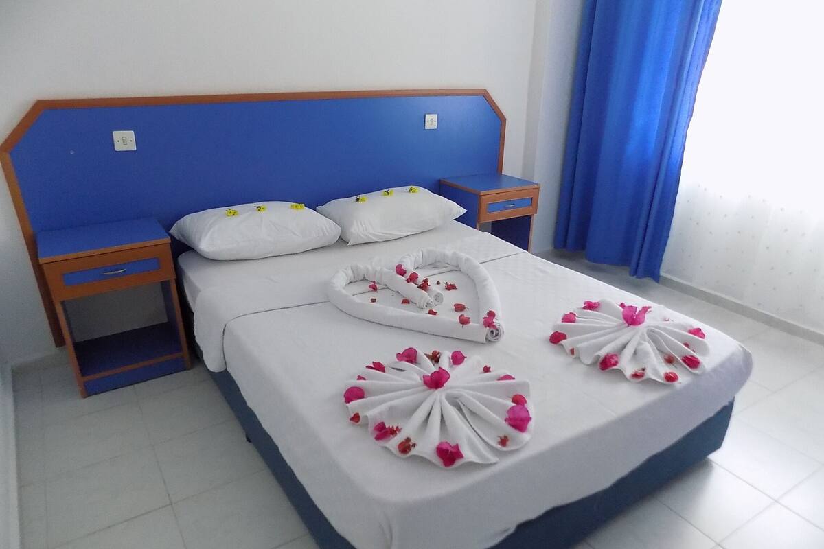 A hotel room with a blue headboard, white bedding, and two towels arranged on the bed.