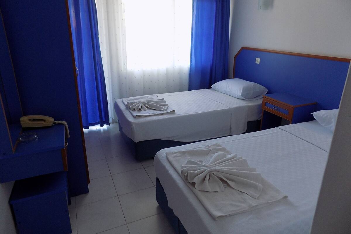 A hotel room with two beds, a wooden headboard, a bedside table with a lamp, and a telephone.