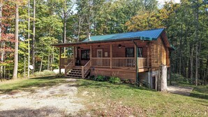 A wooden cabin with a porch and a covered deck, surrounded by trees. - Incredible secluded cabin featuring amazing forest views off of the back deck! (Laurelville)