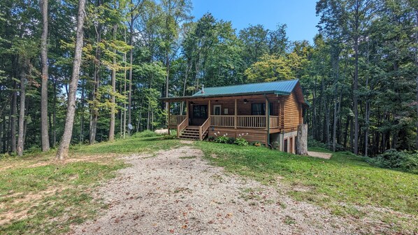 Eine Hütte mit Veranda und einem Kiesweg, umgeben von einem Wald.