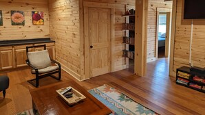 A wooden interior with a chair, a small table, a bookshelf, and a door leading to another room. - Incredible secluded cabin featuring amazing forest views off of the back deck! (Laurelville)