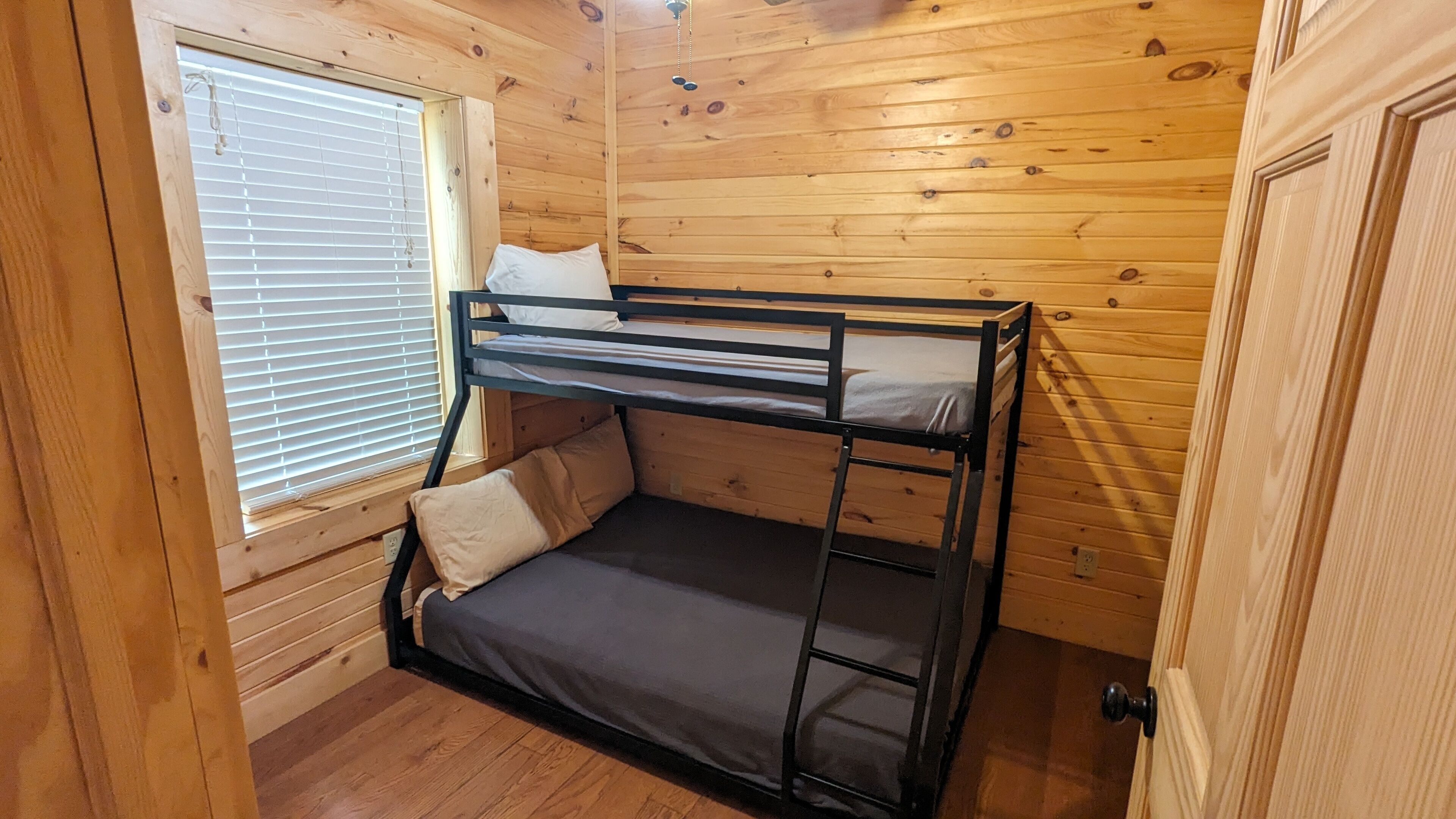 Uma cama de solteiro em um quarto de cabana de madeira, com janela e porta.