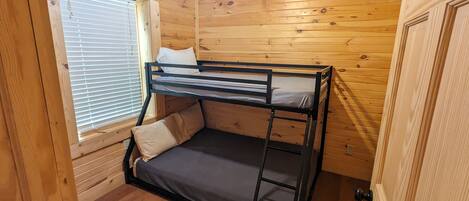 Uma cama de solteiro em um quarto de cabana de madeira, com janela e porta.