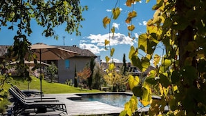 A swimming pool with lounge chairs, a wooden deck, and a house with a tiled roof in the background.
