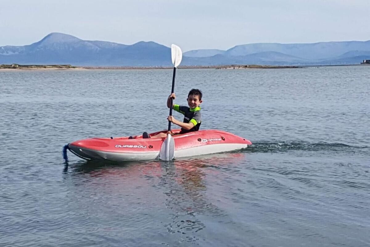 Une personne dans un kayak rouge et blanc sur une étendue d’eau, avec des montagnes en arrière-plan.