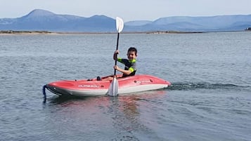 Une personne dans un kayak rouge et blanc sur une étendue d’eau, avec des montagnes en arrière-plan.